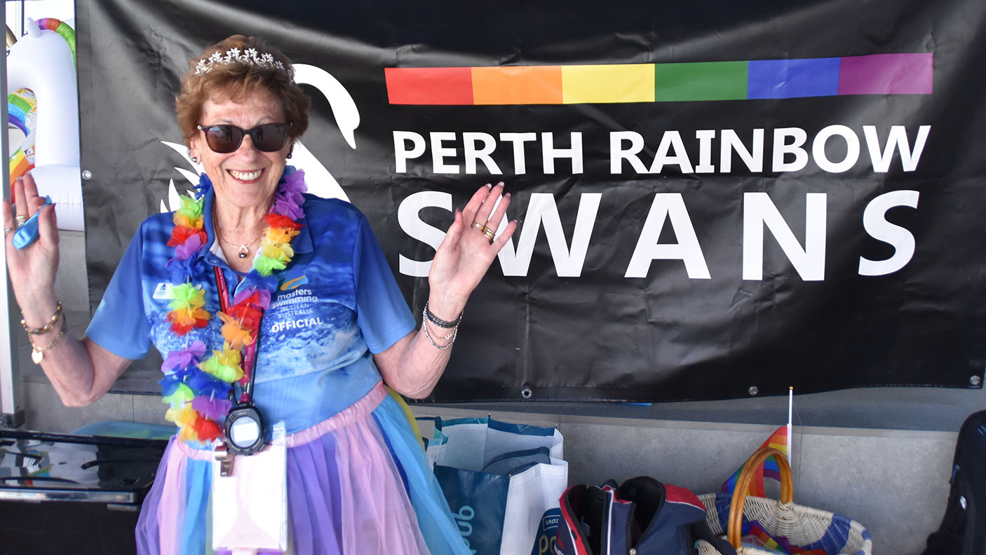 A woman in colourful attire stand in front of the Perth Rainbow Swans banner