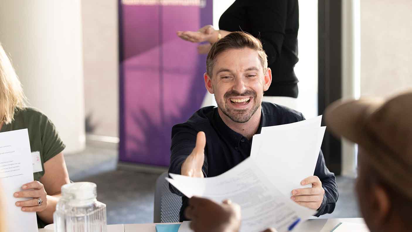 A man holding some paper while seated at a desk