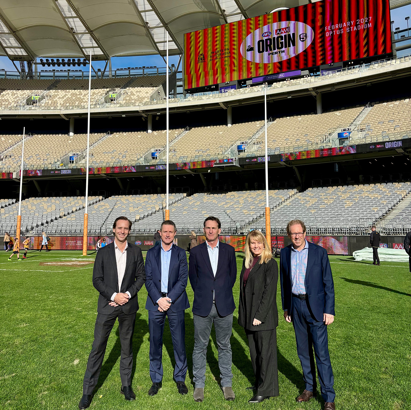 5 people in suits stand on a football pitch in a stadium