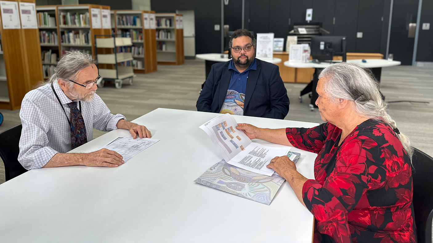 Staff and a visitor sit at a table at the State Library discussing family history