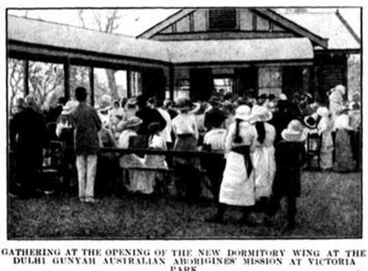 A historical photographh showing a group of people standing at an event in attire and hats of the day. Circa 1915