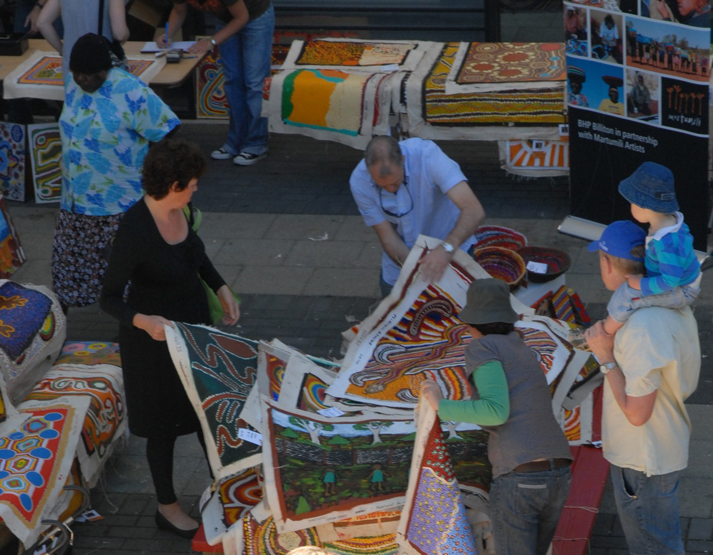 People at an Aboriginal art market, sort through and view stacks of paintings on unframed canvas