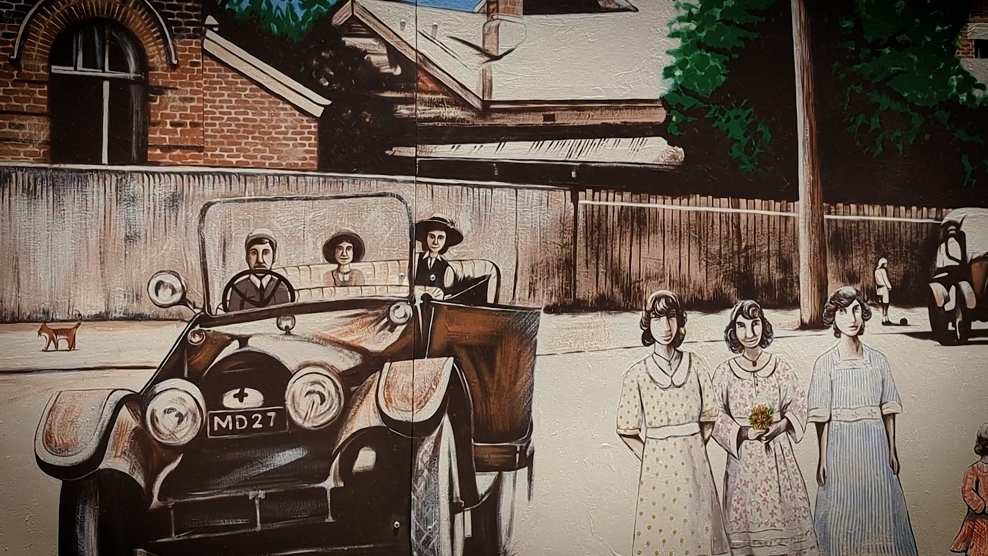 A outdoor mural showing an old car with passengers and people on a street