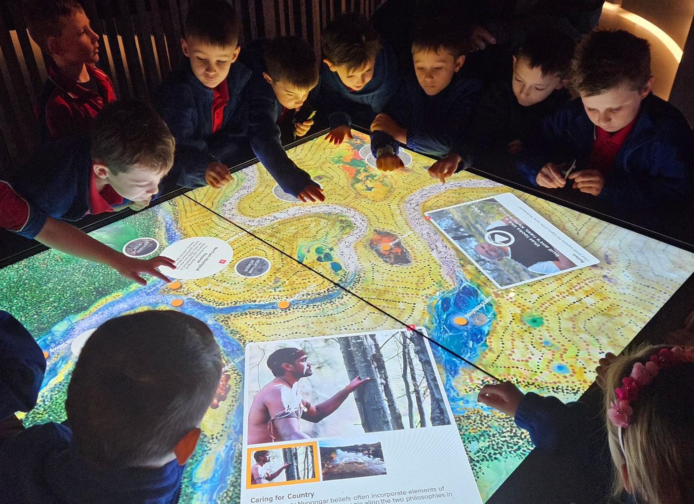 A group of primary school student gather around a backlit artwork on a table