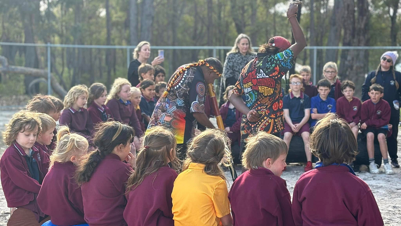 A group of primary school children sit around a yarning circle with an Aboriginal elder in the centre