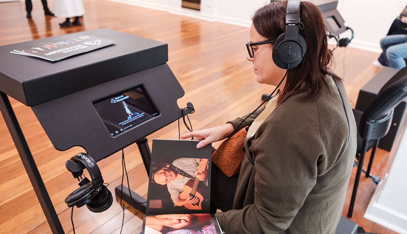 A woman sits in an art gallery looking through a book, with headphones on