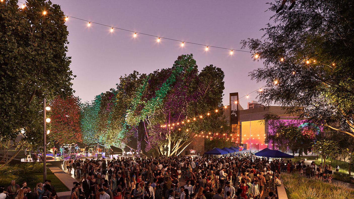 An outdoor event at night. There is a large crowd, coloured lights and a stage.