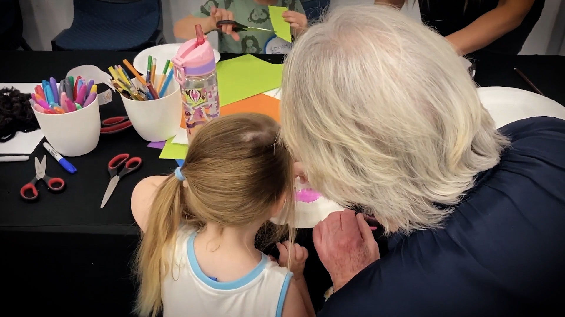 A young child and an older person work on a visual art piece together.