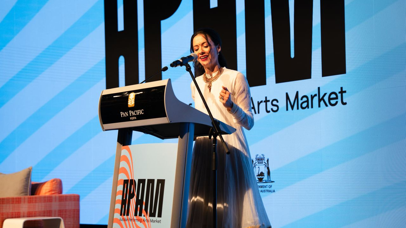 Artist Isha Sharvani standing at a lecturn on the stage at the Australian Performing Arts Market