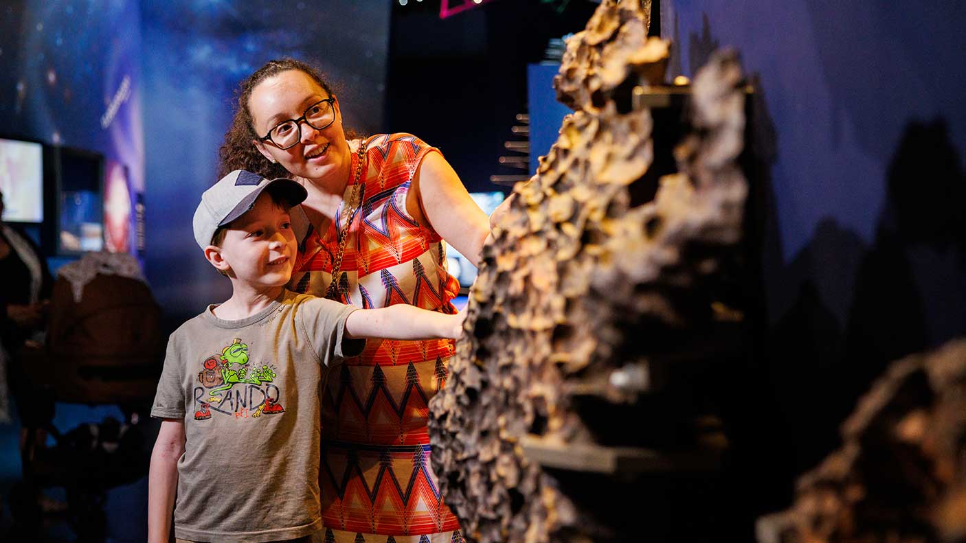 A boy and his mum looking at a meteorite at a museum