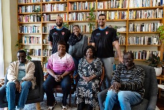 A group of people both sitting on chairs and standing in front of a library of books.