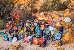 A group of people holding their woven rugs near some rocks.
