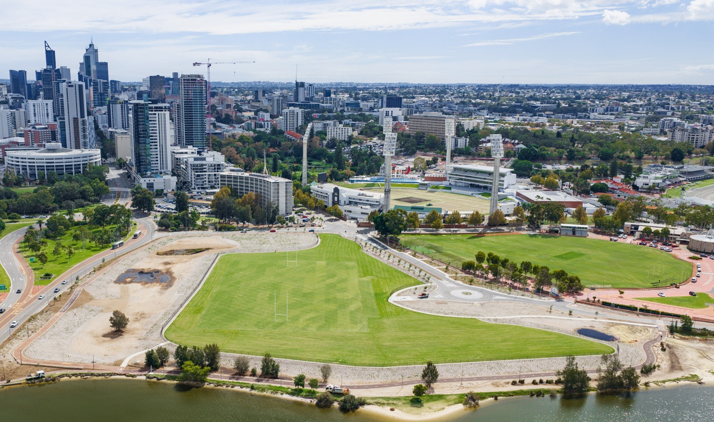 Aerial view of Waterbank with Perth’s city skyline and East Perth riverside precinct, showing open green playing fields