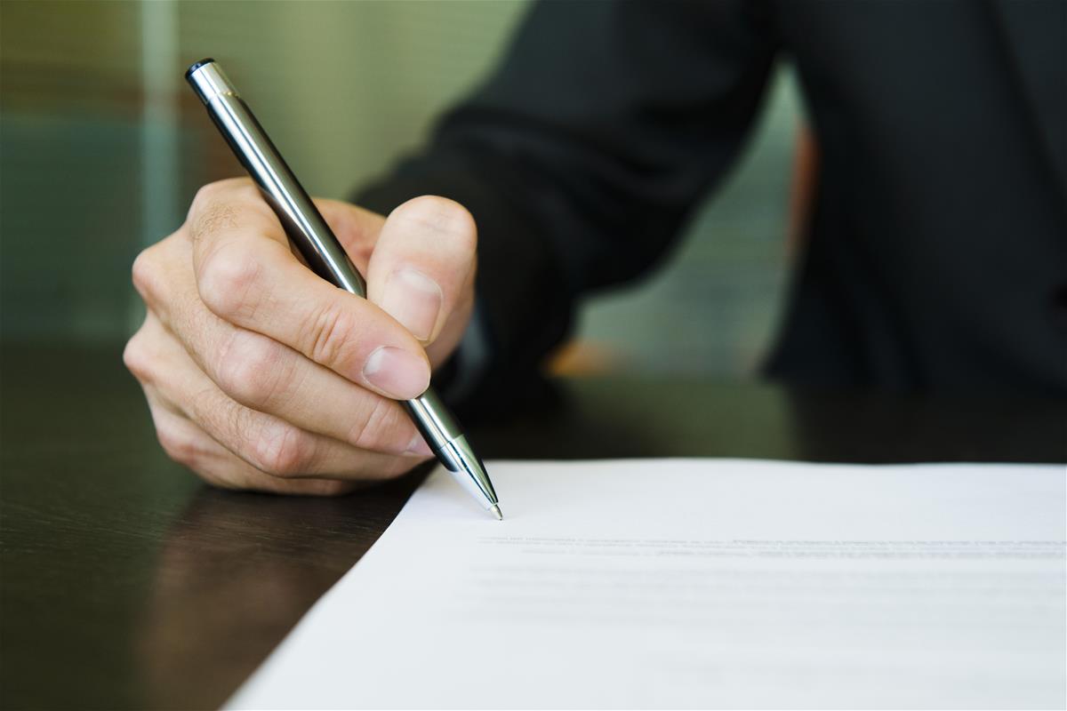 Person signing a document with a pen