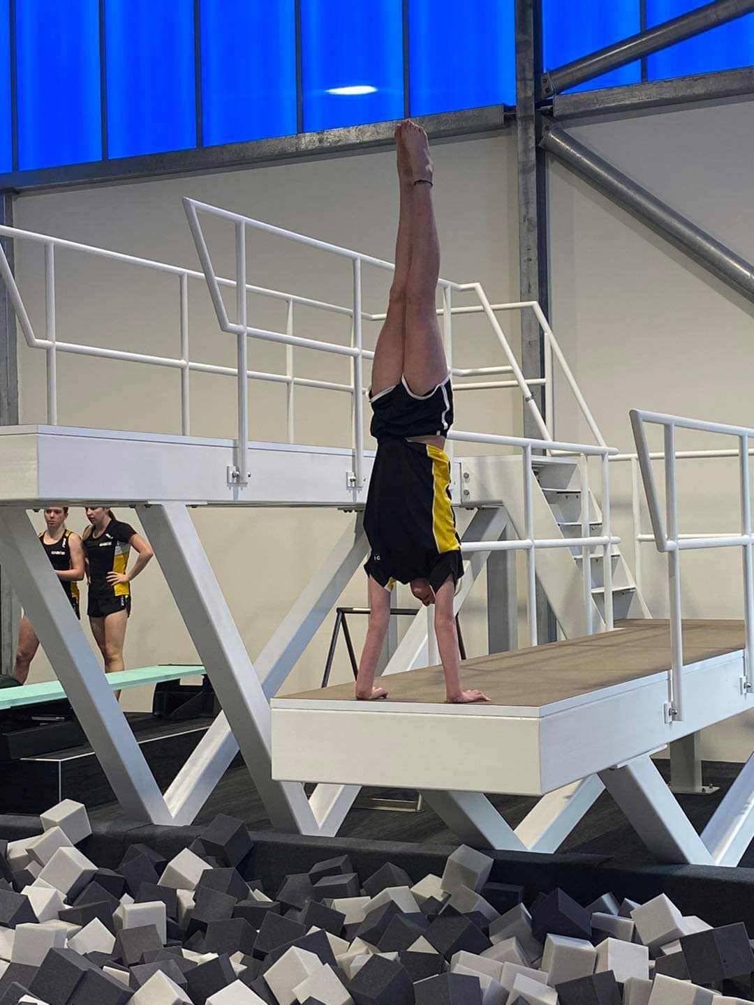 A diver practising their technique, doing an handstand on a platform with a pit of foam blocks below.