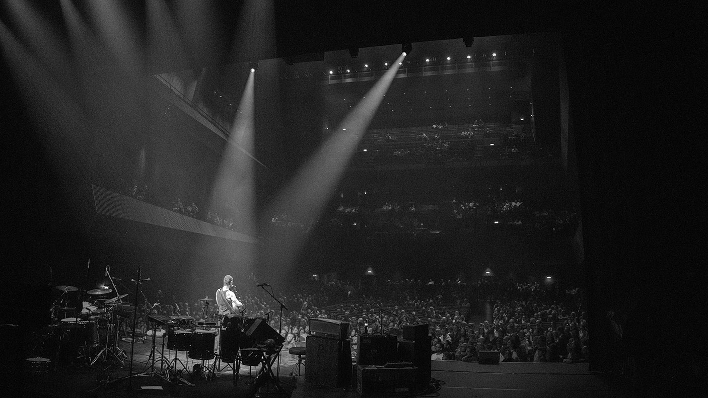 A musician on stage with two spotlights on him. This photo is black and white.