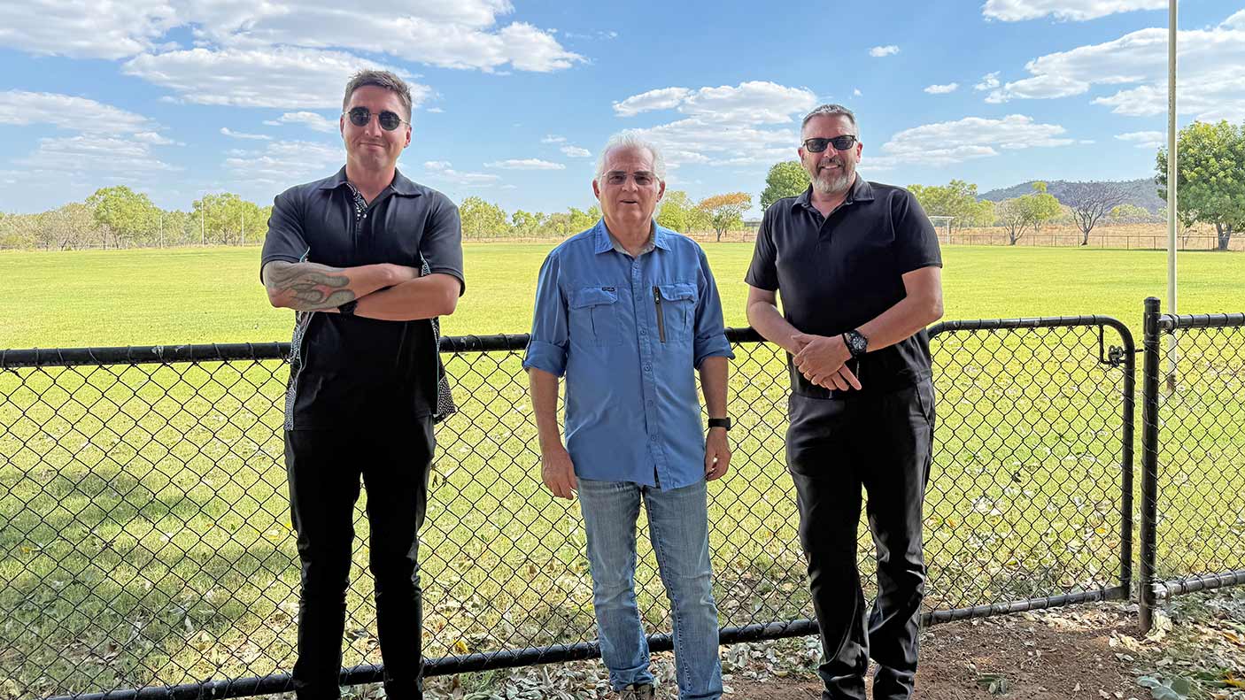 3 men standing in front of a fence at the Warmun Community Oval.