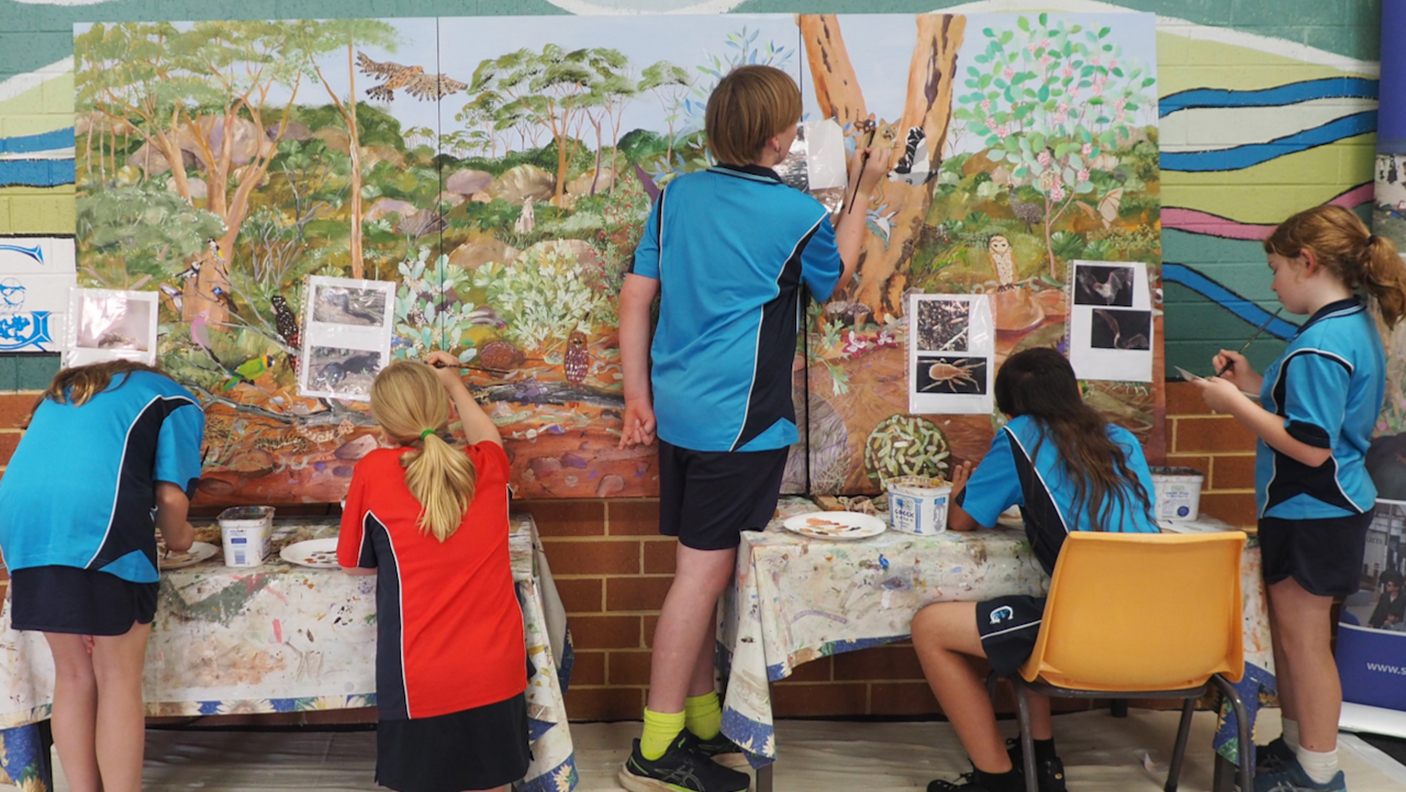 A group of high school students are painting on a large canvas.