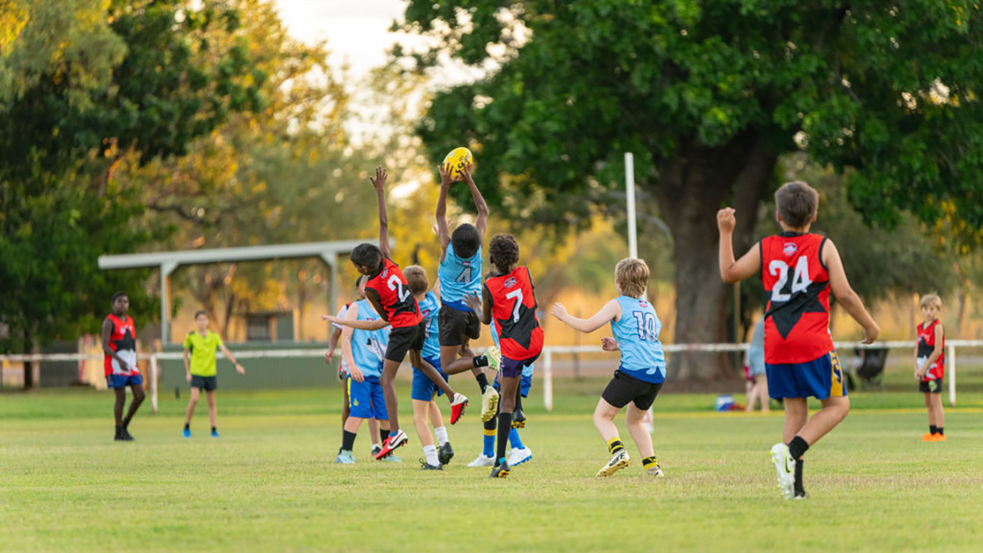 A group of young people playing football on a grassed oval