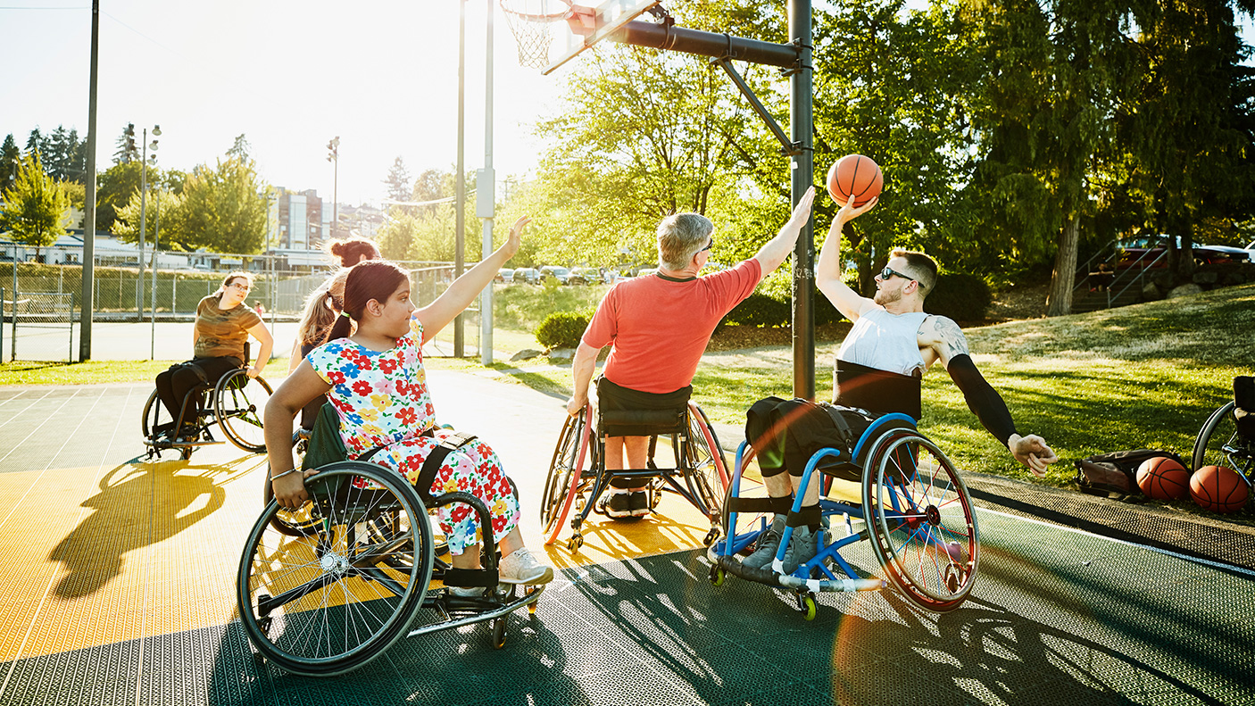 A small group of people in wheelchairs playing basketball on an outdoor court.