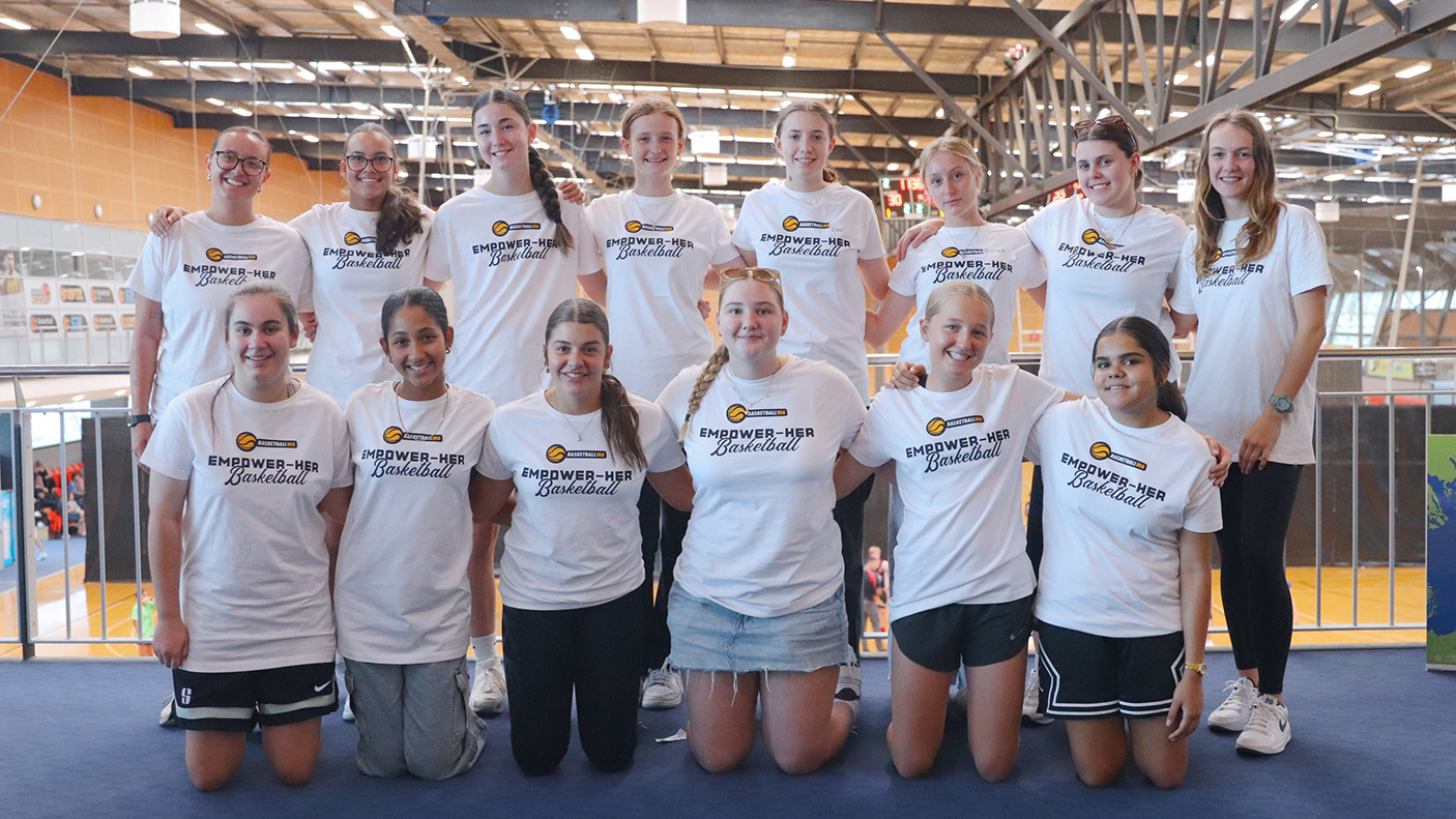 14 basketball players pose for a team photo on a indoor court.