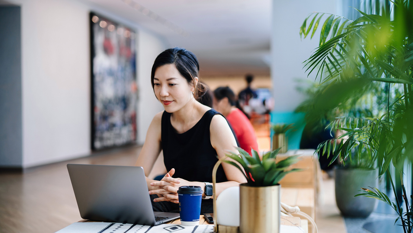 A woman looks at a laptop screen whilst sitting in a cafe