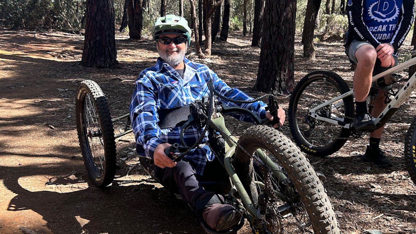 A man on an  adaptive mountain bike, on a forest trail.