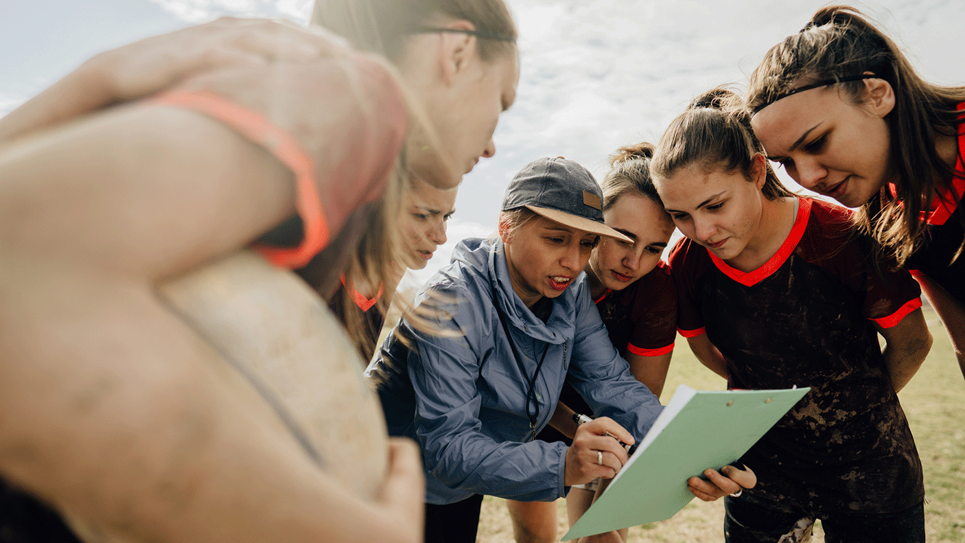 A female coach huddles with a sporting team