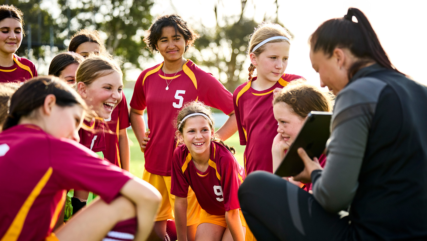 A female coach huddles with her team of school age children