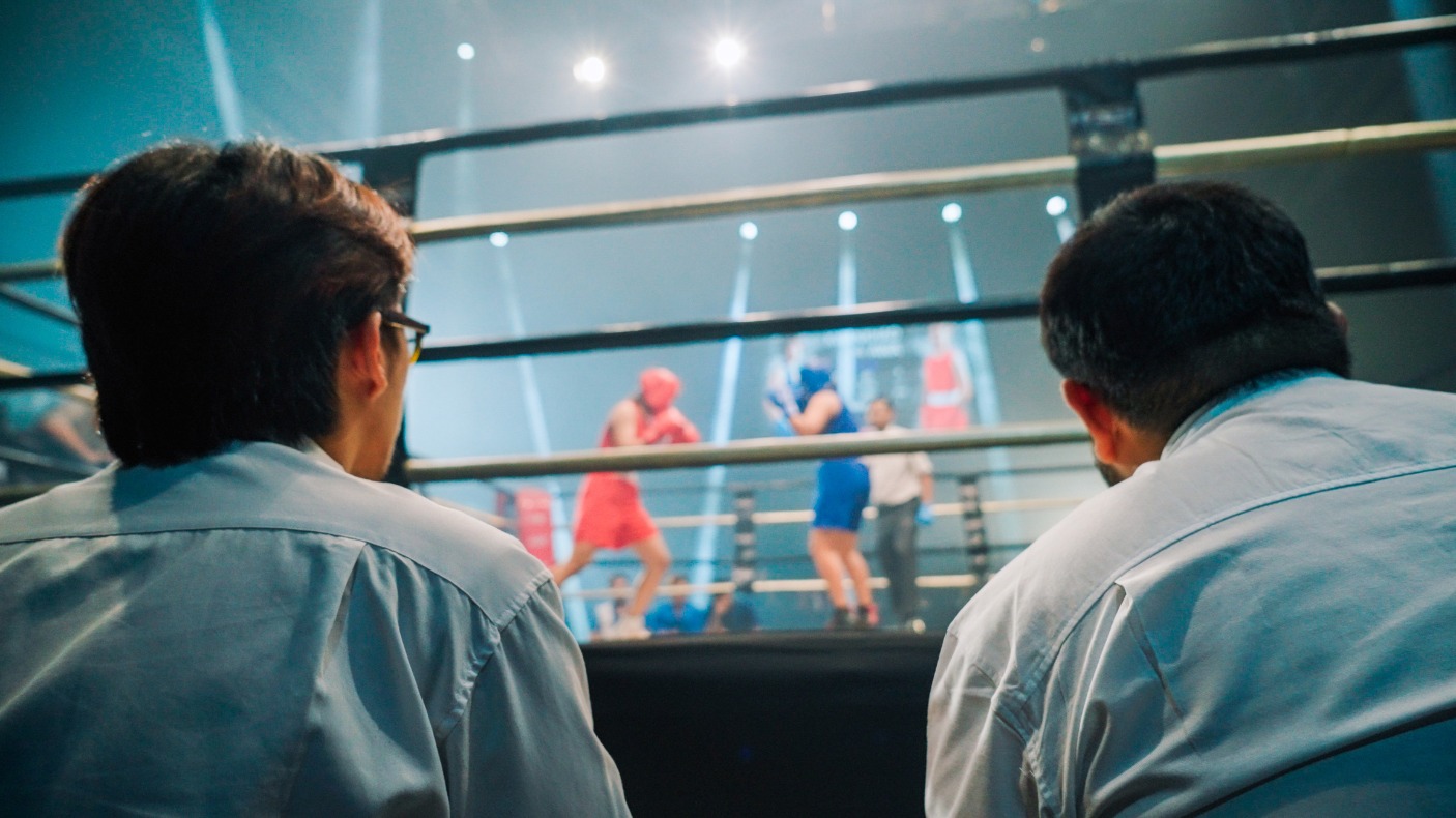 Combat sport doctors sitting ringside watching a boxing event with two boxers in the ring - Stock photo