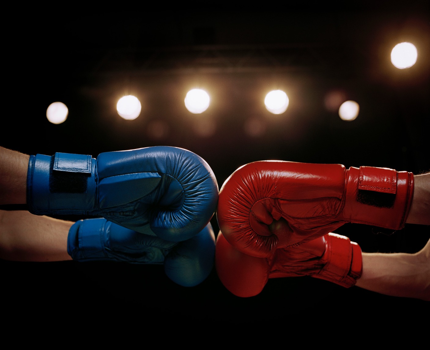 Combat sports athletes touching boxing gloves with cropped hands in red and blue gloves surrounded with stage lights - Stock photo