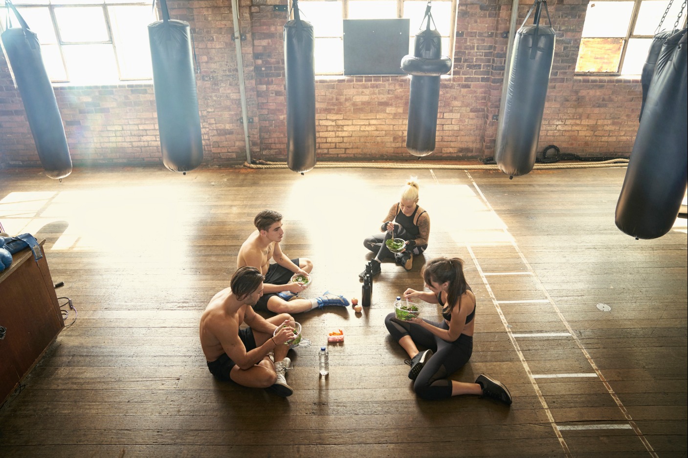 Combat sports athletes sitting in gym eating health food and surrounded by punching bags - stock photo