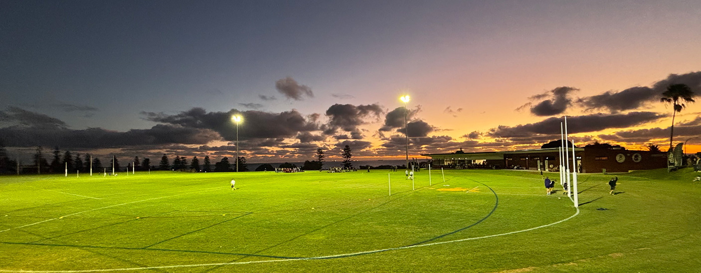 Image of the green turf at Cottesloe oval with the orange glow of a sunset in the background