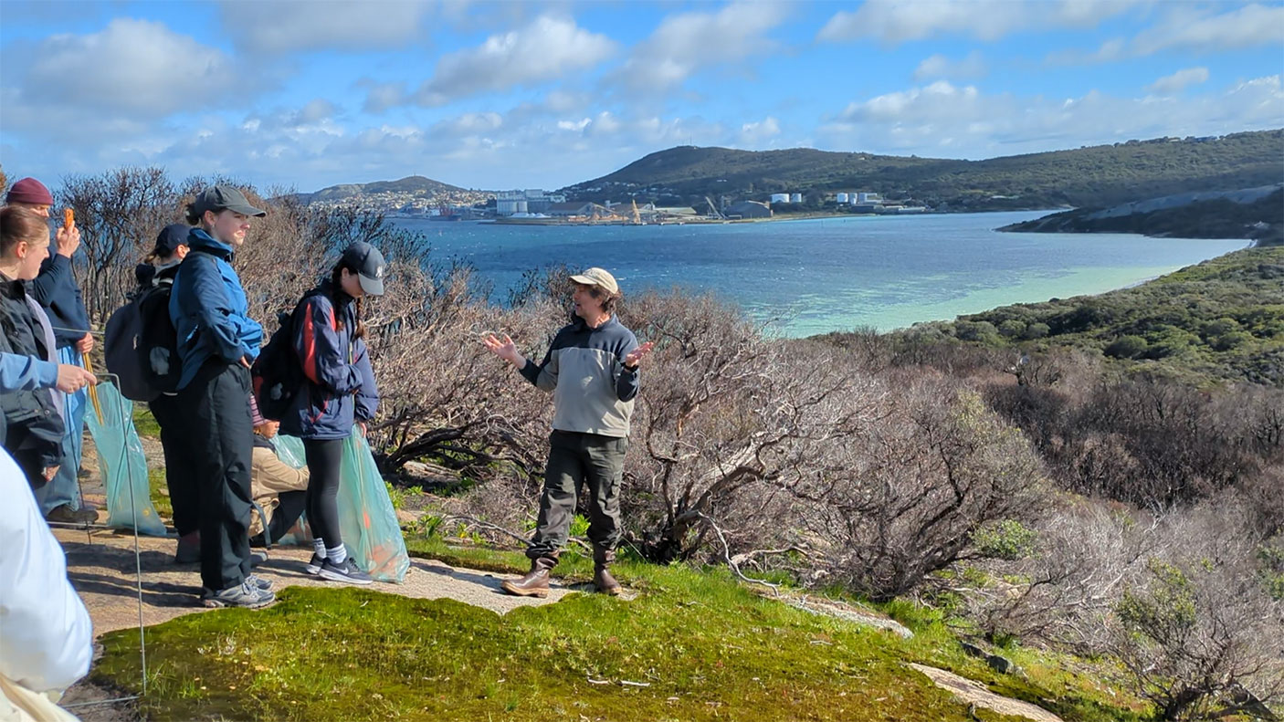 a group of students  gather on a hill overlooking the ocean and coast bushland