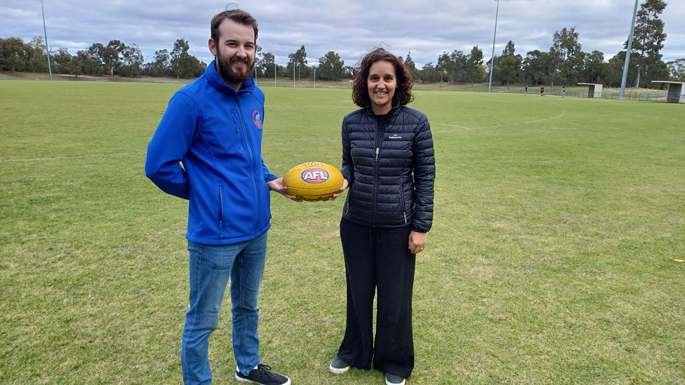 2 adults stand on a grassy field with a football in their hands.