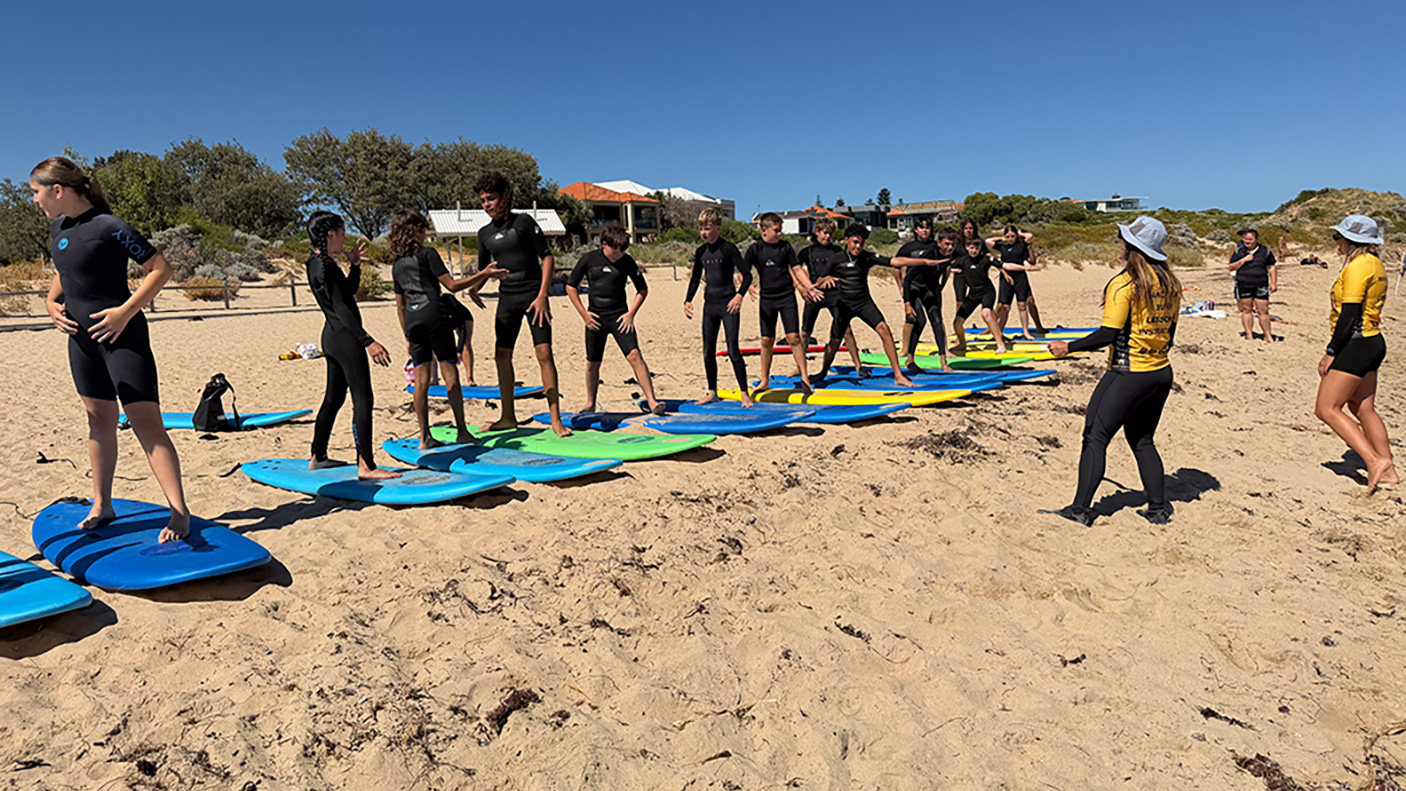 A group o school students stand on surfboards, on the beach with instructors, during a surfing lesson