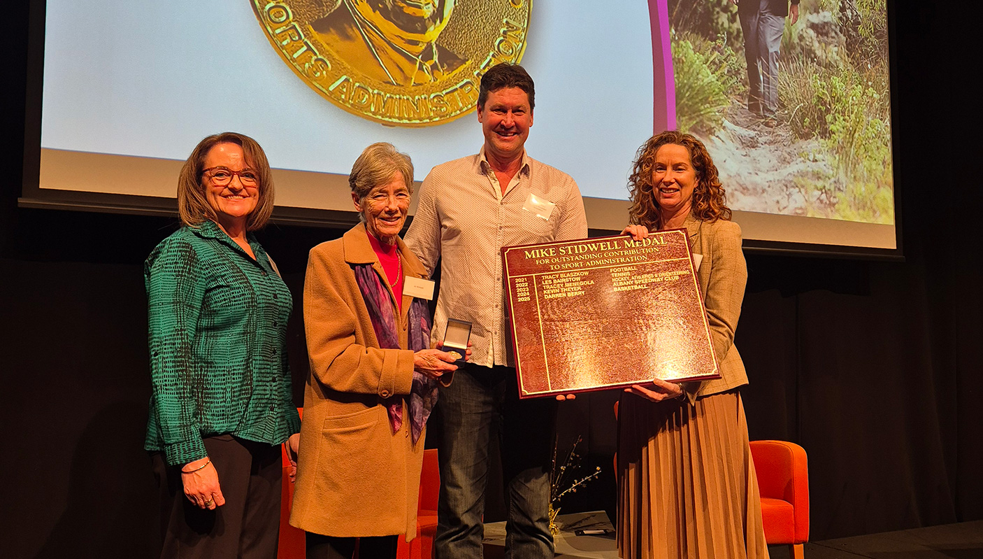 Three people stand with Mike Stidwell medal winner 2026