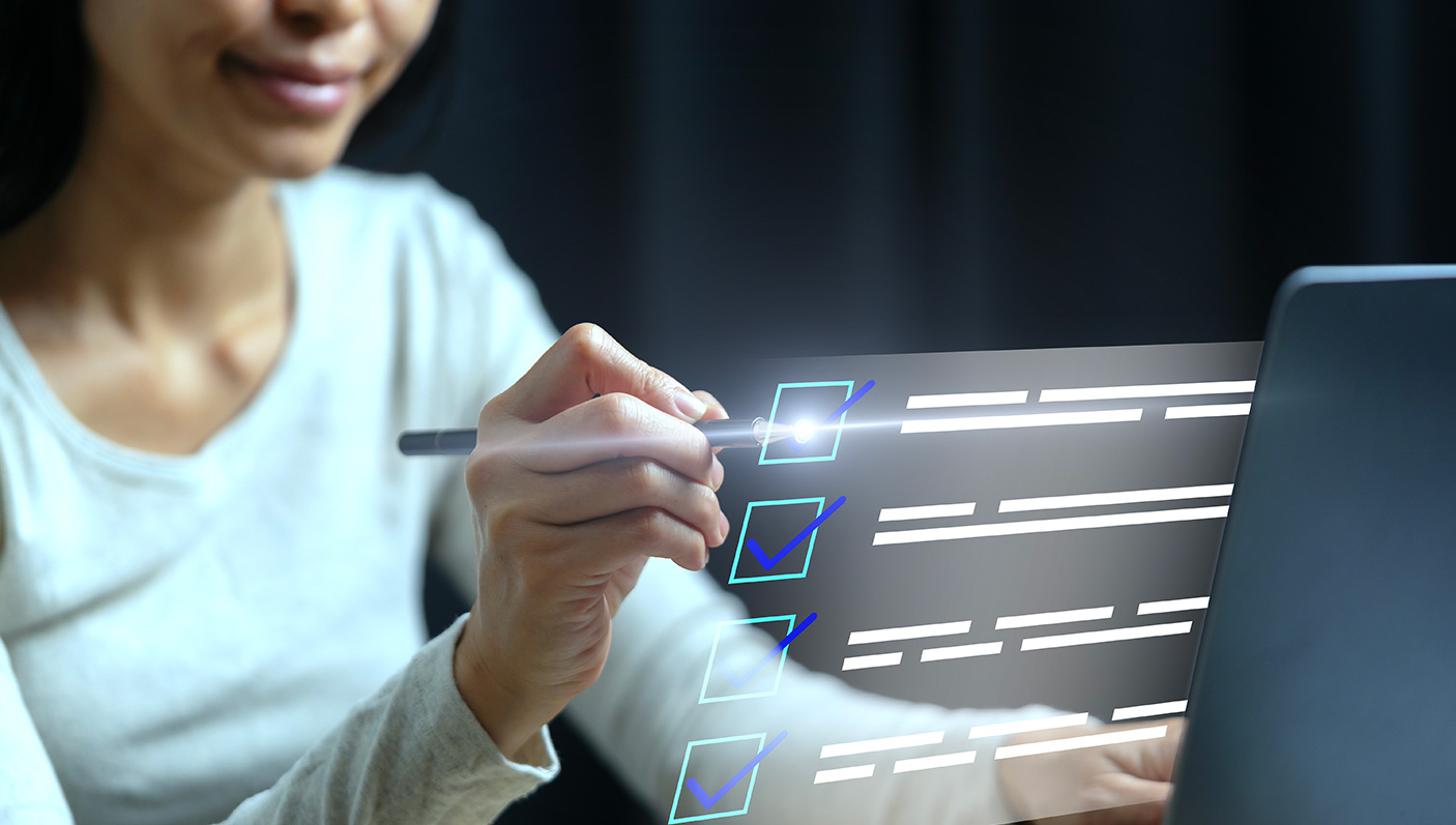 A woman holds a stylus, ticking checkboxes on a laptop