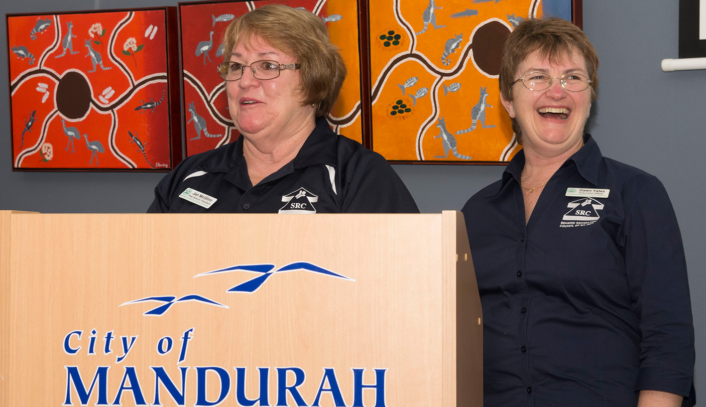 2 women stand at a lecturn, which has the City of Mandurah on it.