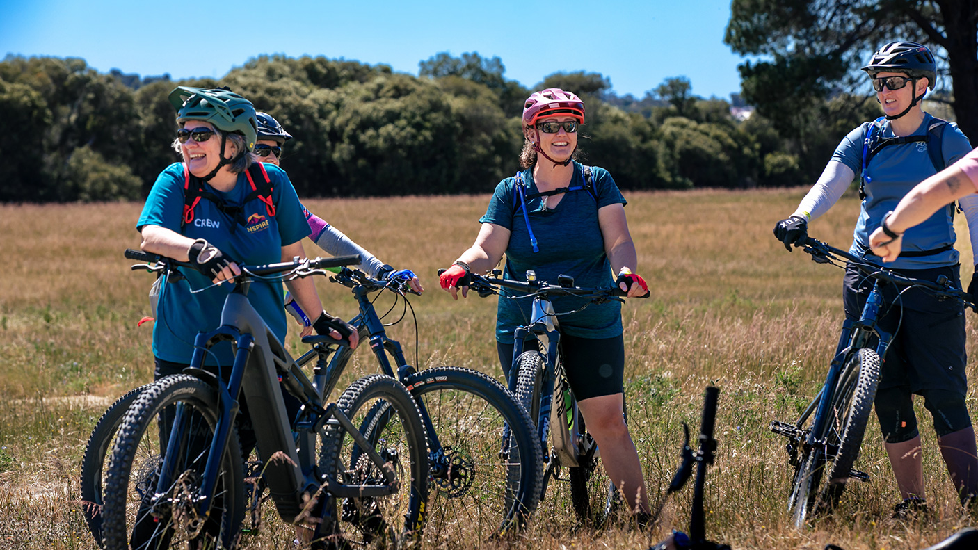 A small group of women standing with their mountain bikes, talking and laughing in a off-road landscape.