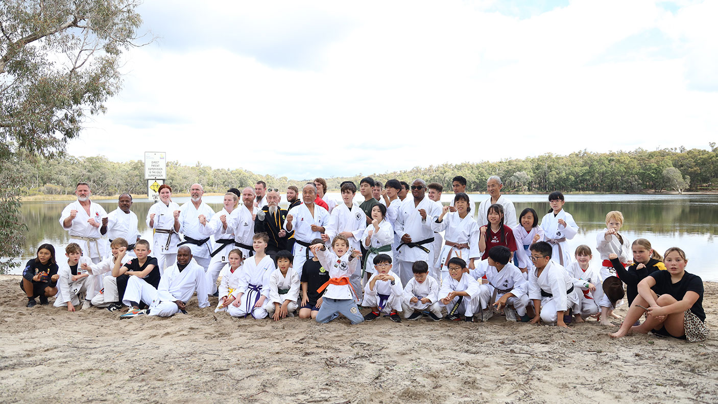 A group of people wearing Karate attire stand by the edge of a lake