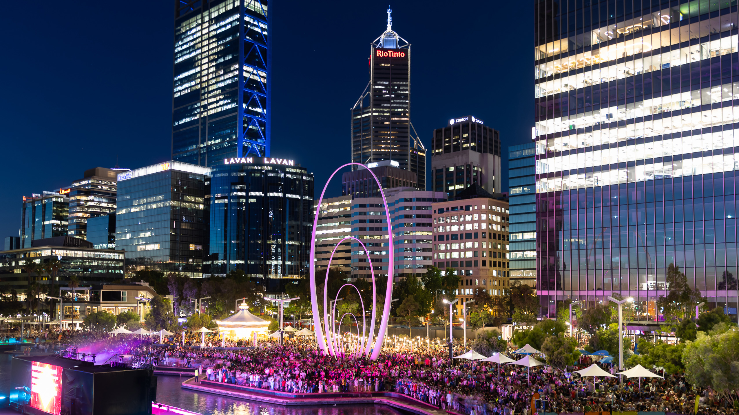 Crowd gathered at Elizabeth Quay for a night-time event with Perth city buildings illuminated in the background