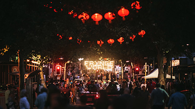 Arts festival crowd gathered along a street at night beneath red lanterns and illuminated event signage