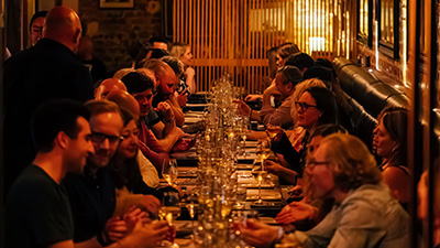 Guests seated along a long communal table in a warmly lit restaurant during a shared dining event.