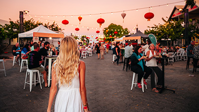 Visitors gather at an outdoor evening event with food stalls, seating areas and red lanterns strung overhead